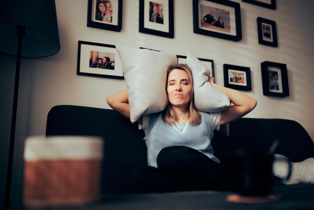 woman,sitting,on,a,sofa,covering,her,ears,with,pillows.